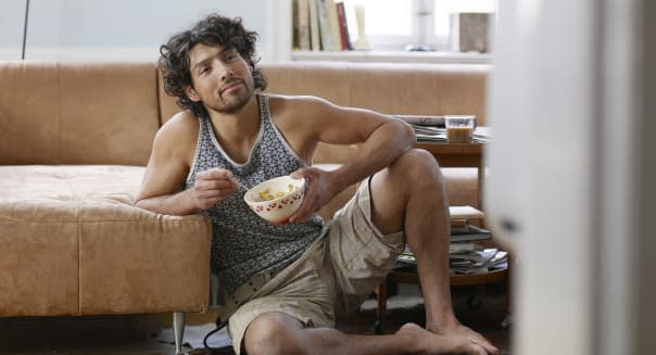 Young man sitting on floor, eating breakfast