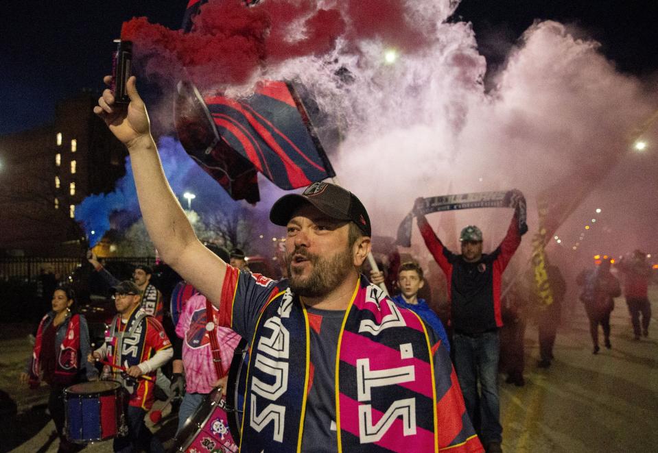 Jeremy Eckstein carries a smoke bomb as fans march to CityPark stadium for the first St. Louis City SC home MLS soccer game, against Charlotte FC, Saturday, March. 4, 2023, in downtown St. Louis. (Christine Tannous/St. Louis Post-Dispatch via AP)