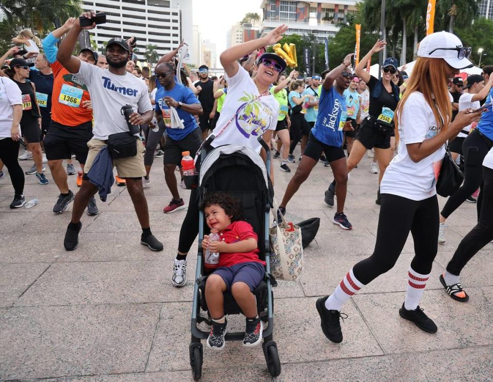 A Runner exercises during a warm up session before the start of the race as her unhappy companion cries in the stroller.