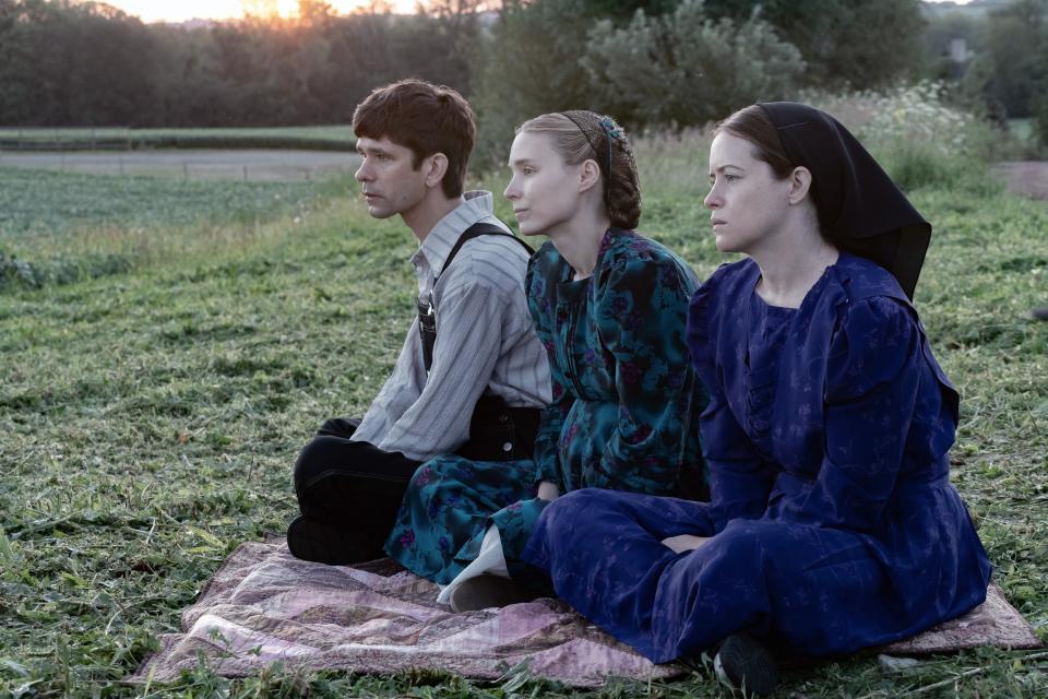 Ben Whishaw, Rooney Mara, and Claire Foy sit on a rug looking into the distance