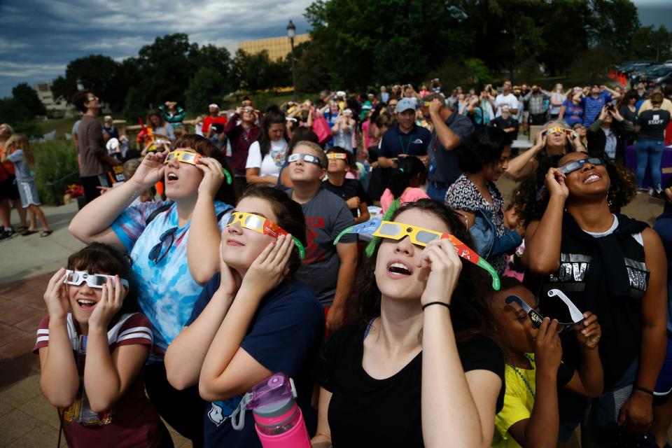 Eclipse watchers look up as the clouds break and the beginning of the eclipse starts to become visible Monday, Aug. 21, 2017, during a solar eclipse watch party hosted by the Science Center of Iowa outside the Iowa State Capitol in Des Moines.
