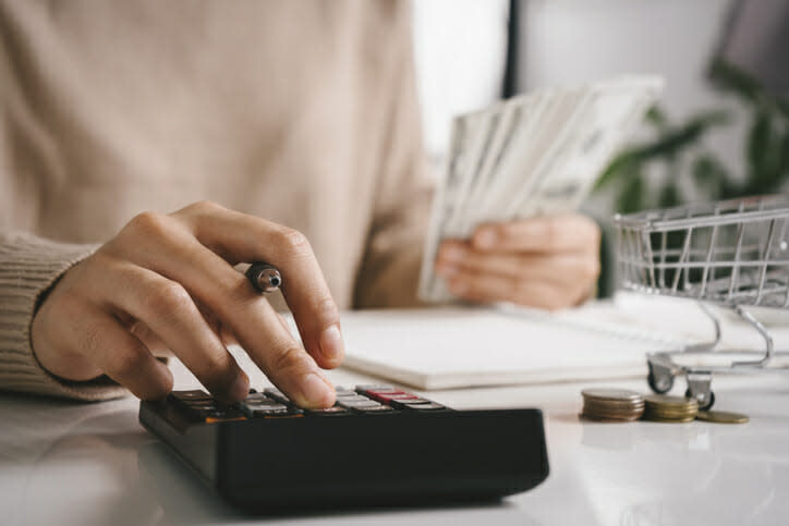 A woman's hand holds a pen while using a calculator and holding money in the other hand.