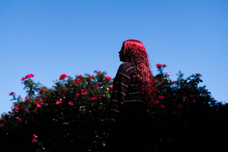 Sharon stands in the park next to bright pink flowers.