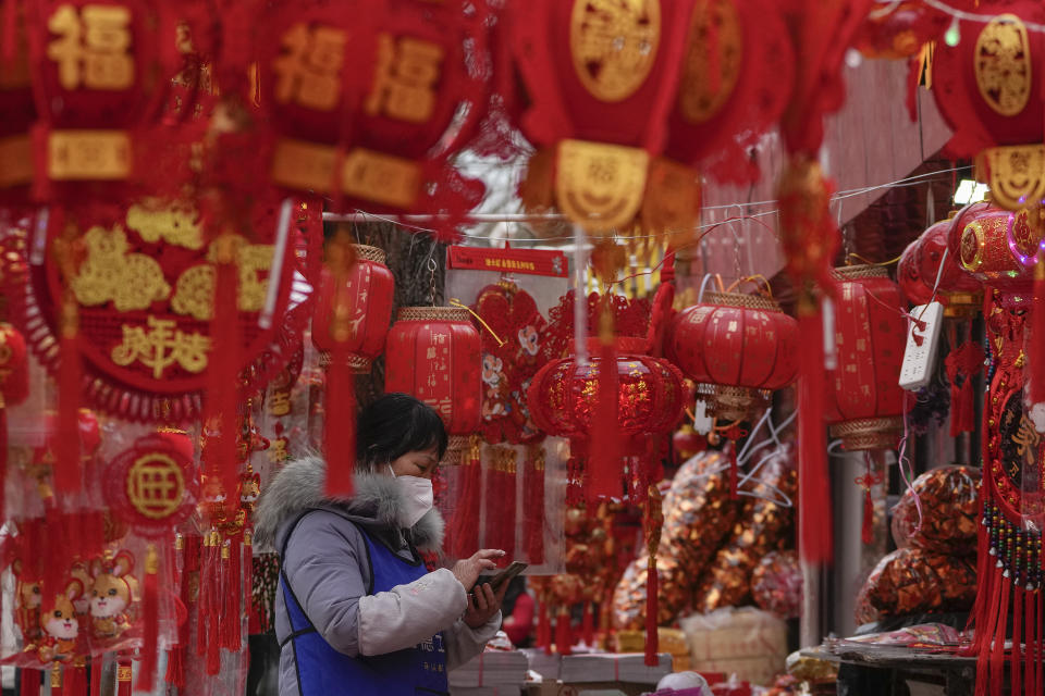 A vendor wearing a face mask checks her smartphone at her store selling Chinese Lunar New Year decorations in Beijing, Saturday, Jan. 7, 2023. China has suspended or closed the social media accounts of more than 1,000 critics of the government's policies on the COVID-19 outbreak, as the country moves to further open up. (AP Photo/Andy Wong)
