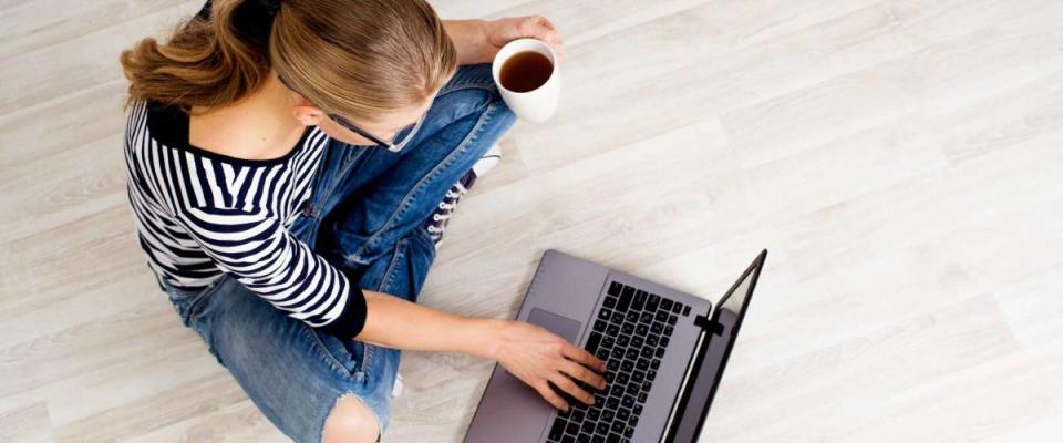 Ecommerce woman. Young female using computer for online shopping, sitting on the floor and drinking coffee.