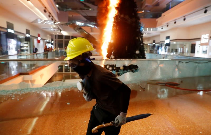 A protester runs next to a burning Christmas tree at Festival Walk mall in Kowloon Tong, Hong Kong