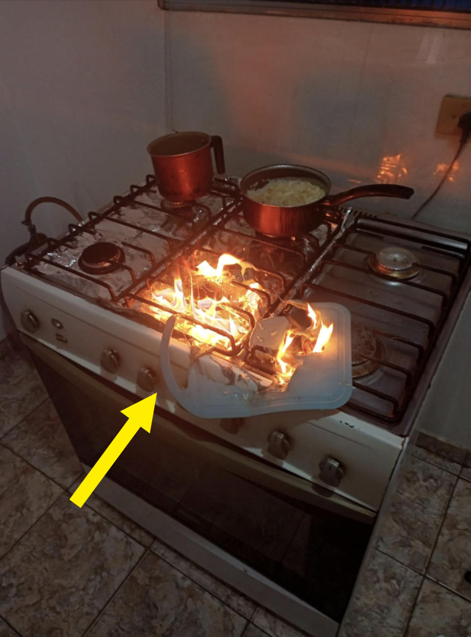 A stove fire with flames on the right side of the stovetop, with pots on back burners and it appears a plastic object has caught fire in front