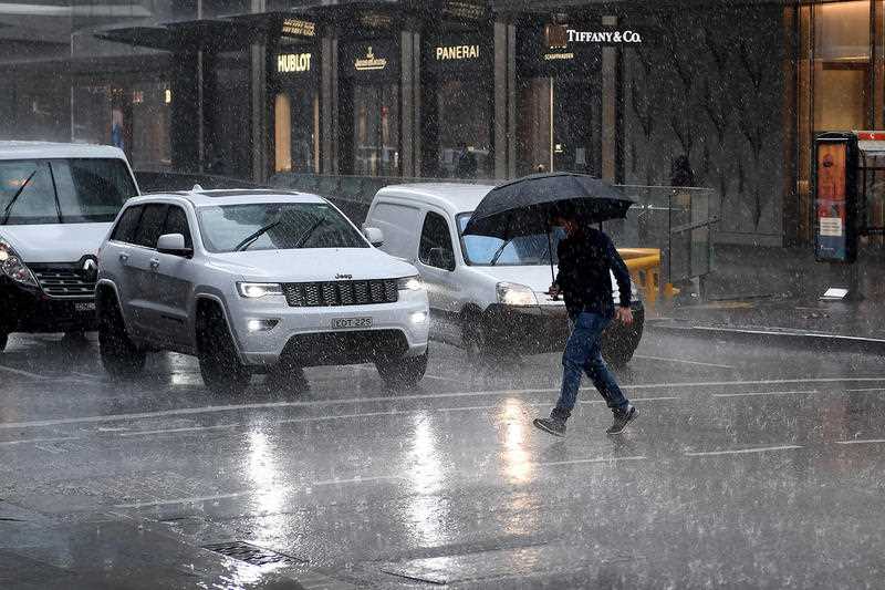 People are seen as heavy rain falls briefly in the central business district of Sydney.