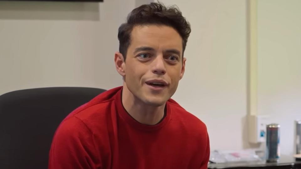 Rami Malek wearing a red sweater looking forward on SNL.