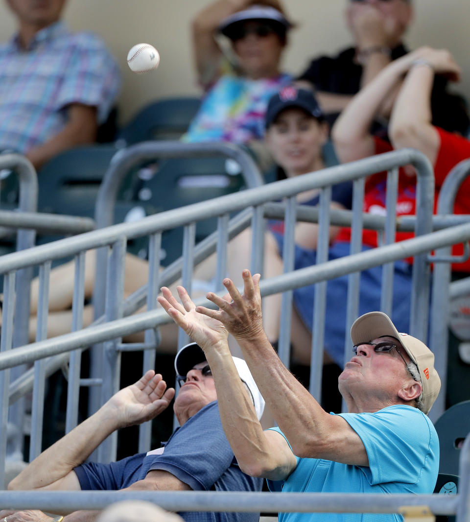 A fan eyes a foul ball from the Miami Marlins during the eighth inning of a spring training baseball game against the Miami Marlins, Tuesday, March 10, 2020, in Jupiter, Fla. The ball fell between the two men and bounced away. (AP Photo/Julio Cortez)