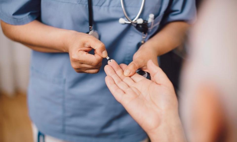 A nurse taking a patient’s blood sugar reading. Posed by models.