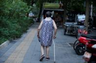 An elderly woman walks with a stick along a street in downtown Beijing