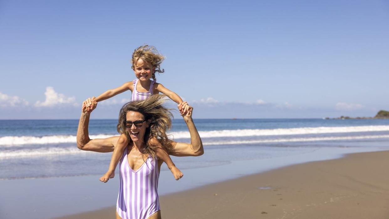 a mother and daughter in matching swim suites running towards the ocean in costa rica