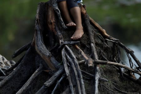 The feet of an Indigenous girl from the Parintintin tribe are seen as she sits on a cut tree trunk in Traira village near Humaita