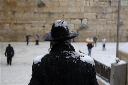 A man stands in front of the Western Wall as snow falls in Jerusalem's Old City December 12, 2013. REUTERS/Darren Whiteside