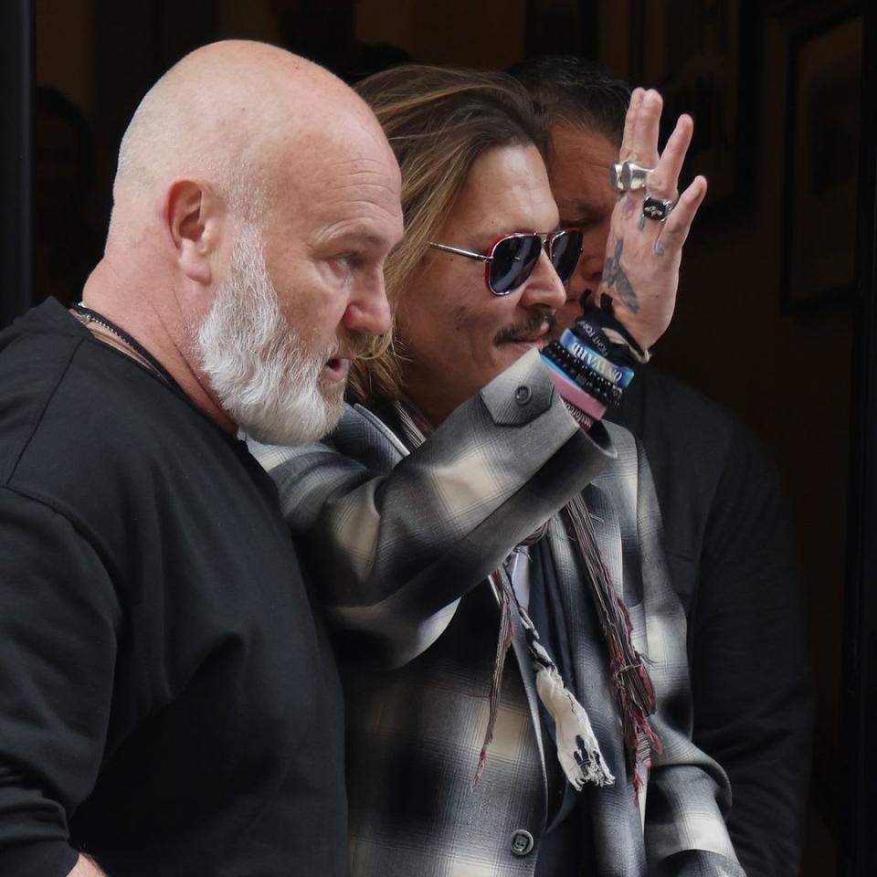 Johnny Depp waving to crowds as he is guided by a security guard