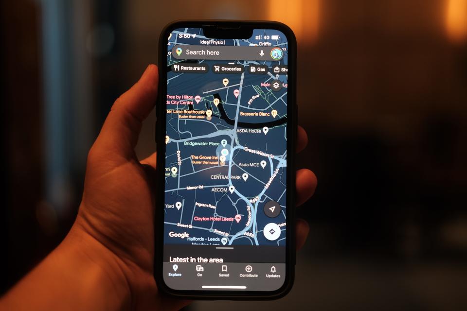 A hand holding an iPhone with Google Maps displayed on the screen.