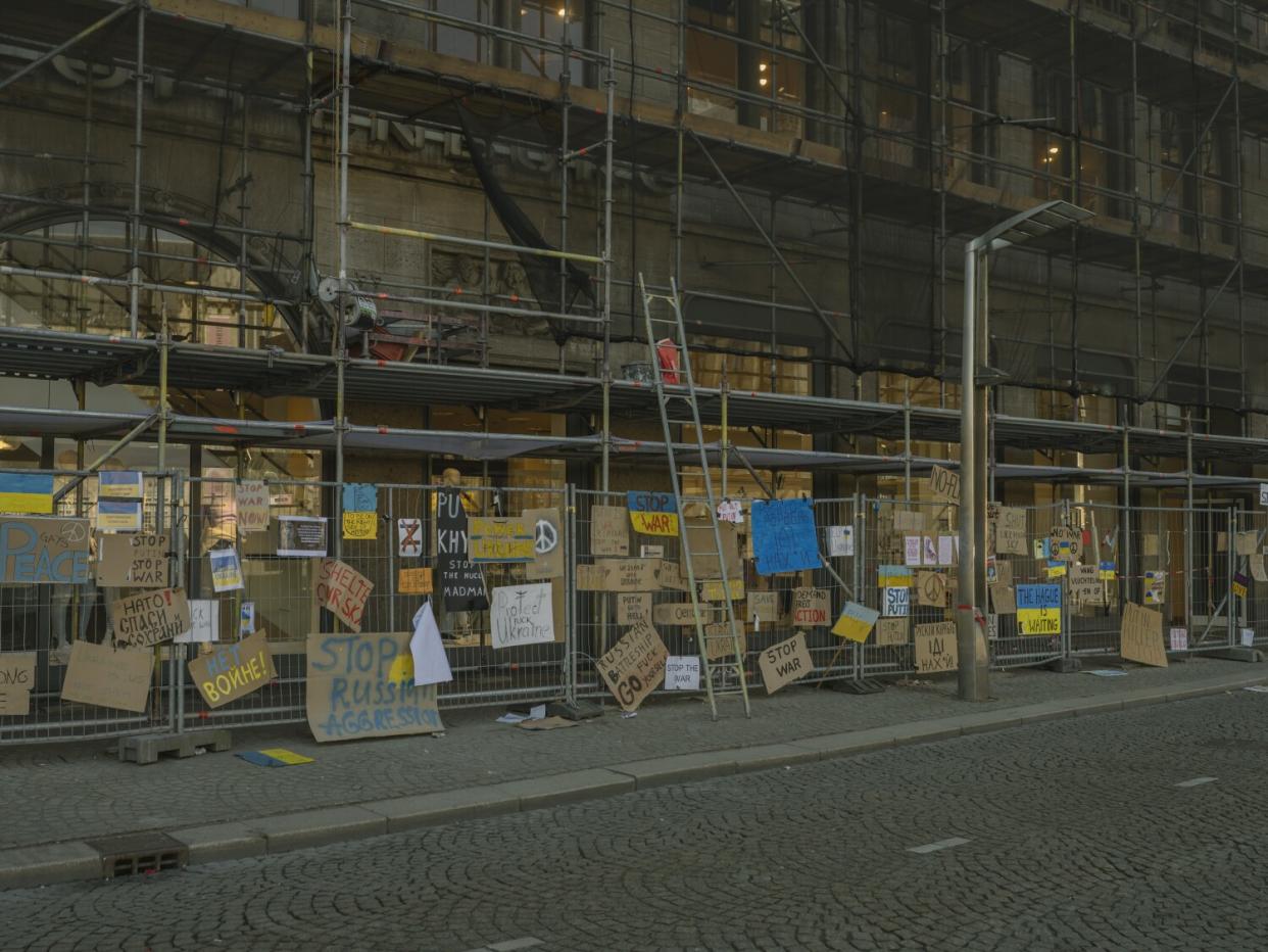 Many cardboard signs are hung on a fence below scaffolding