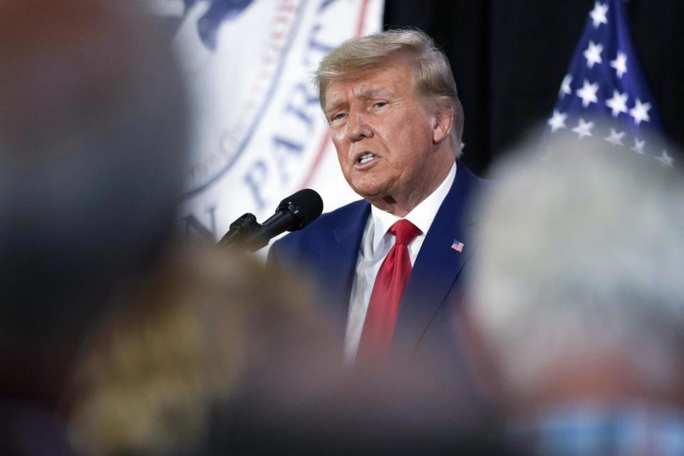 Former President Trump talking into a microphone, framed by the backs of audience members' heads