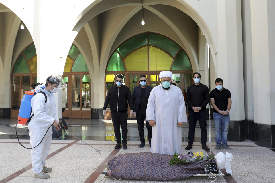 A technician sprays disinfectant as mourners pray over the body of a person who died from COVID-19, at the Behesht-e-Zahra cemetery on the outskirts of the Iranian capital, Tehran, Iran, Sunday, Nov. 1, 2020. Behesht-e-Zahra, or "Zahra's Paradise" in Farsi, was named after a daughter of the Prophet Muhammad. (AP Photo/Ebrahim Noroozi)