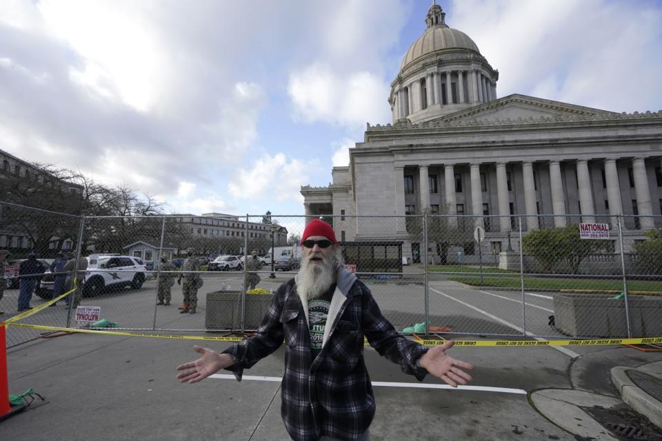 Rickie Day stands outside a perimeter fence at the Capitol in Olympia, Wash. National Guard members and police stand inside.