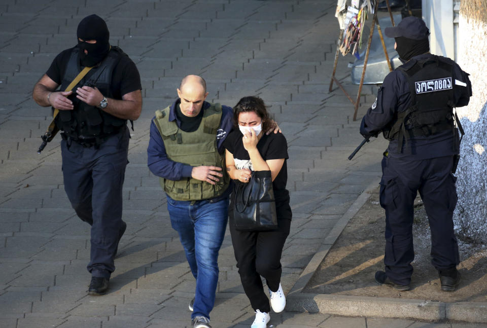 Georgian police officers escorts a woman who escaped from a bank where an armed assailant has taken several people hostage, in the town of Zugdidi in western Georgia, Wednesday, Oct. 21, 2020. An armed assailant took several people hostage at a bank in the ex-Soviet nation of Georgia on Wednesday, authorities said. The Georgian Interior Ministry didn't immediately say how many people have been taken hostage in the town of Zugdidi in western Georgia, or what demands the assailant has made. Police sealed off the area and launched an operation "to neutralize the assailant," the ministry said in a statement. (AP Photo/Zurab Tsertsvadze)