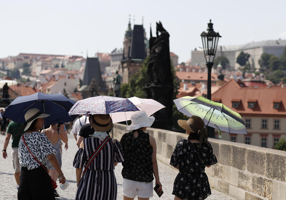 Tourists use umbrellas to shield themselves form the sun as they cross the medieval Charles Bridge on a hot day in Prague, Czech Republic, Wednesday, June 26, 2019. (AP Photo/Petr David Josek)