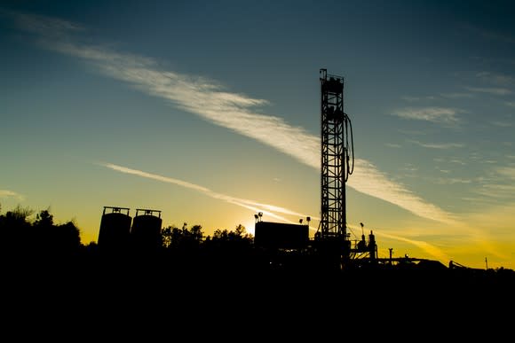 Drilling rig at sunrise on a clear day, with equipment nearby.