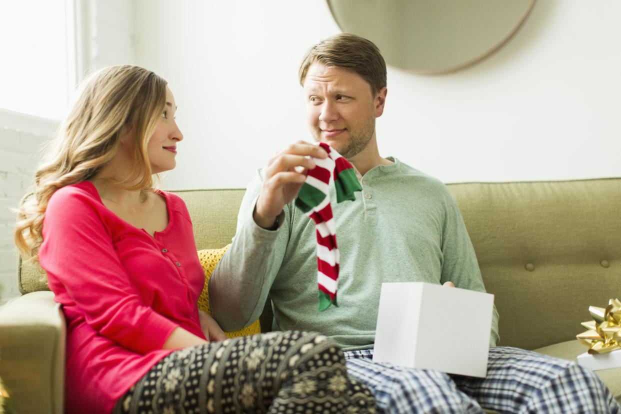 Man receiving unwanted Christmas presents from partner, holding socks up. (Getty Images)