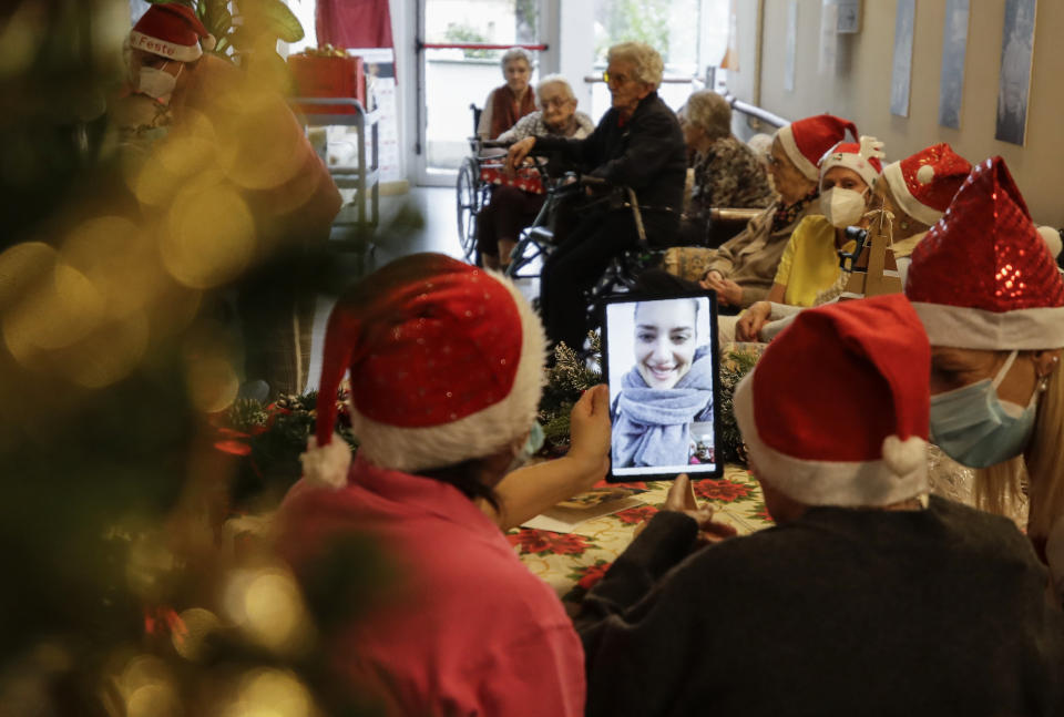 Pasqualina Ghilardi, center, is flanked by carer Michela Valle, left, and director Maria Giulia Madaschi, as she talks on a video call with Caterina Damiano, a donor unrelated to her, who bought and sent her a Christmas present through an organization dubbed "Santa's Grandchildren", at the Martino Zanchi nursing home in Alzano Lombardo, one of the area that most suffered the first wave of COVID-19, in northern Italy, Saturday, Dec. 19, 2020. (AP Photo/Luca Bruno)