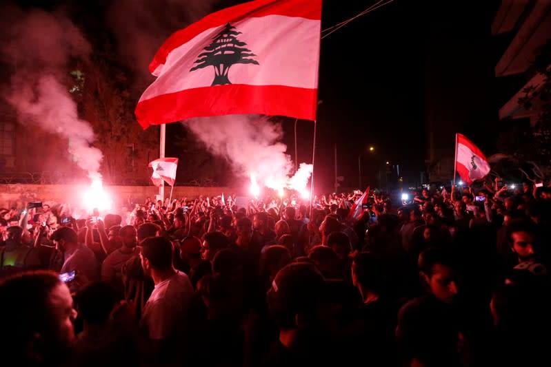 Demonstrators hold flares and Lebanese flags as they protest outside the house of former Lebanese prime minister Fouad Siniora in Beirut