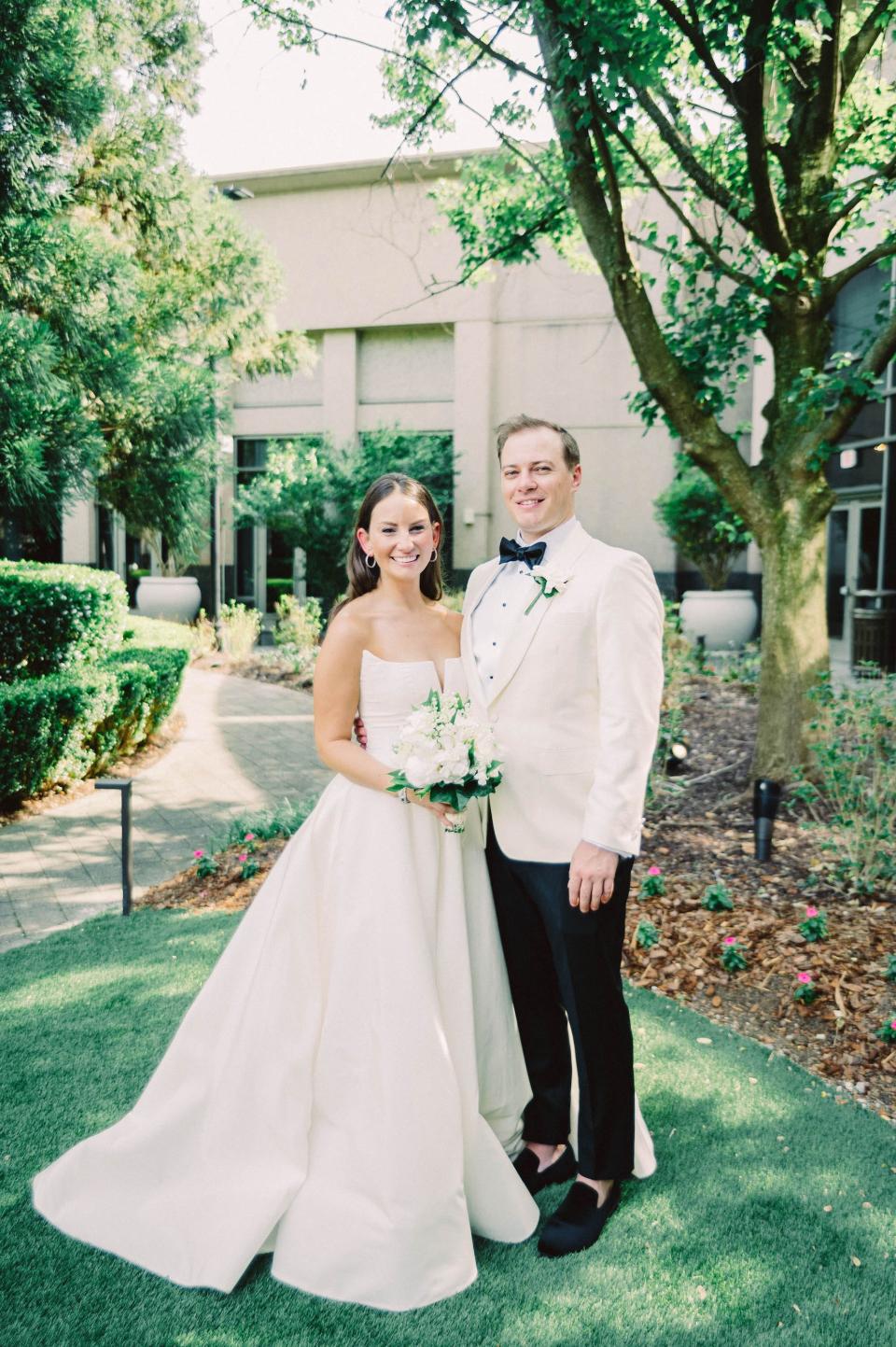 A bride and groom smile for a photo on a lawn.