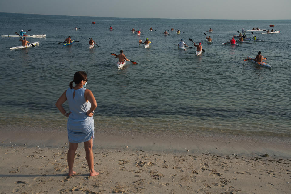 A woman wearing a face mask due to the coronavirus pandemic watches kayak racers take off from the coast of Dubai, United Arab Emirates, Friday, June 19, 2020. Dubai has begun allowing organized sports competitions to take place after locking down over the coronavirus pandemic and the COVID-19 illness it causes. Competitions held Friday at the Dubai Offshore Sailing Club were among the first events to be held. (AP Photo/Jon Gambrell)