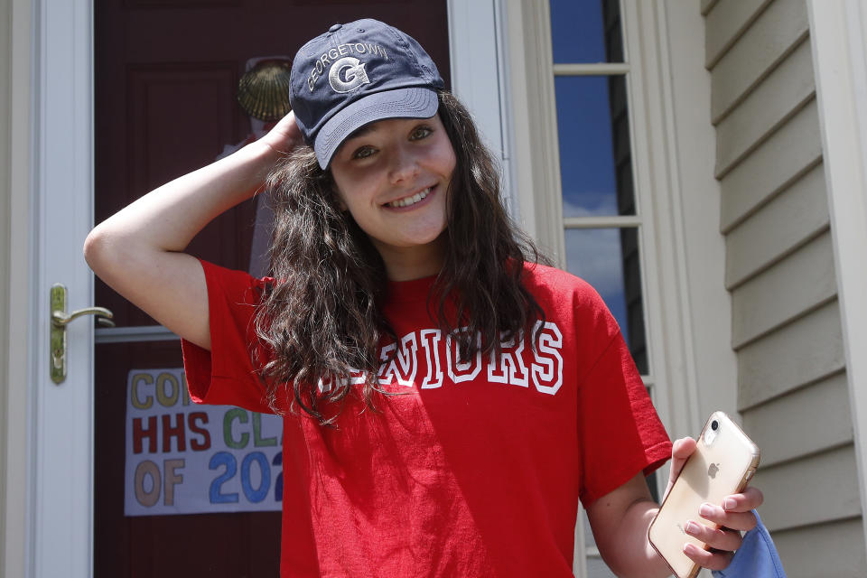 In this June 1, 2020 photo, high school graduate Lizzie Quinlivan wears a Georgetown University cap at her home in Hingham, Mass. Quinlivan has opted to attend closer-to-home Georgetown instead of colleges on the west coast which were on her original wish-list. As students make college plans for this fall, some U.S. universities are seeing surging interest from in-state students looking to stay closer to home amid the coronavirus pandemic. (AP Photo/Elise Amendola)