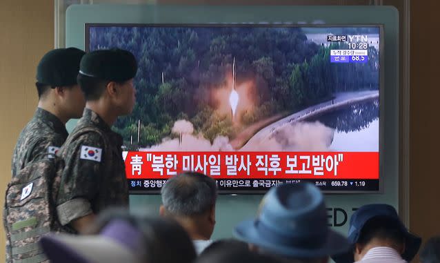 Army soldiers walk by a TV news program showing a file image of a missile being test-launched by North Korea. Source: AP