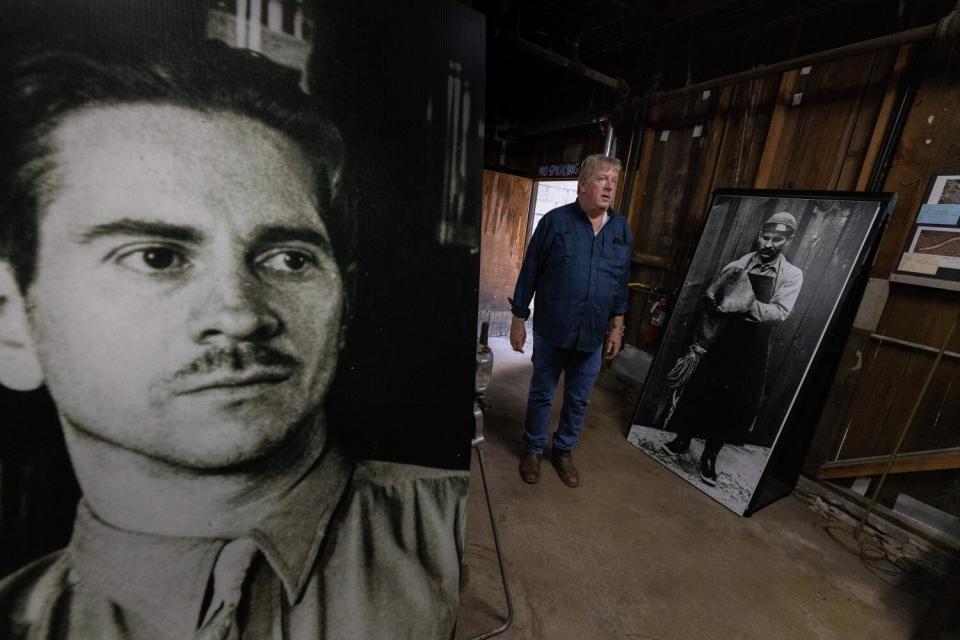 A man stands near the open door of a room that contains two large portrait photos.