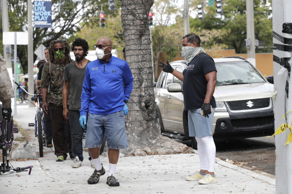 Derek Fleming, right, a business partner with chef Marcus Samuelsson, controls the crowd outside of their Red Rooster Restaurant as people wait in line for a free meal during the new coronavirus pandemic, Monday, April 6, 2020, in the Overtown neighborhood of Miami. Samuelsson has partnered with chef Jose Andres' World Central Kitchen to distribute meals to those in need. (AP Photo/Lynne Sladky)