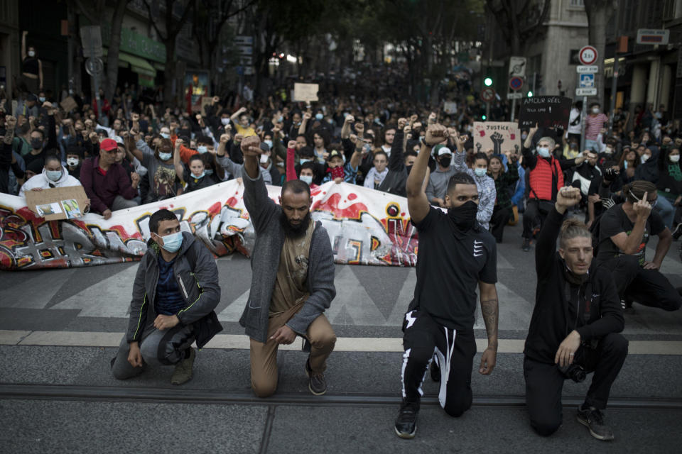 Protesters raise their fists and kneel in front of French riot police during a march against police brutality and racism in Marseille, France, Saturday, June 13, 2020, organized by supporters of Adama Traore, who died in police custody in 2016. Several demonstrations went ahead Saturday inspired by the Black Lives Matter movement in the U.S. (AP Photo/Daniel Cole)