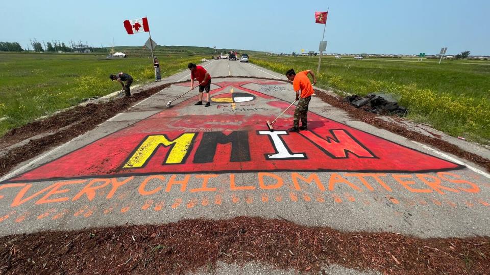 Supporters sweep soil and wood chips off a mural honouring missing and murdered Indigenous women and girls on Sunday after a man dumped the soil from the back of his pickup truck onto the painting.