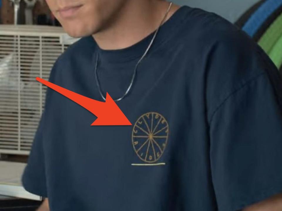 arrow pointing to clydes rides logo on eli shirt in along for the ride