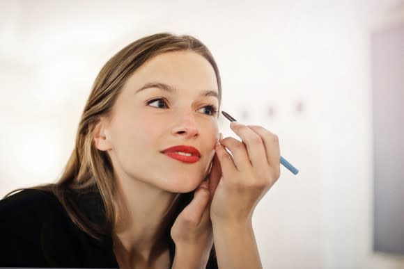 Woman applying eyeliner in front of mirror.