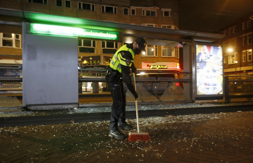A police officer sweeps up glass from a bus stop that was smashed in protests against a nation-wide curfew in Rotterdam, Netherlands, Monday, Jan. 25, 2021. The Netherlands Saturday entered its toughest phase of anti-coronavirus restrictions to date, imposing a nationwide night-time curfew from 9 p.m. until 4:30 a.m. in a bid to control the COVID-19 infection rate. (AP Photo/Peter Dejong)