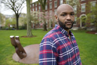 Brown University graduate Jason Carroll, a Maryland native whose ancestors were slaves in the Carolinas, stands for a portrait on the Brown campus in Providence, R.I., on Tuesday, May 4, 2021, near the Slavery Memorial, left, by sculptor Martin Puryear erected in 2014. Nearly two decades after launching its much-lauded reckoning with slavery, Brown hasn't taken any meaningful steps to compensate slave descendants themselves, argues Carroll. (AP Photo/Steven Senne)