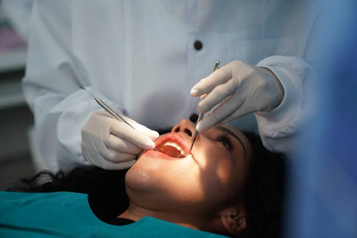A dentist is performing a dental check-up on a patient lying back in a chair. The dentist is wearing gloves and using dental tools to examine the patient's teeth
