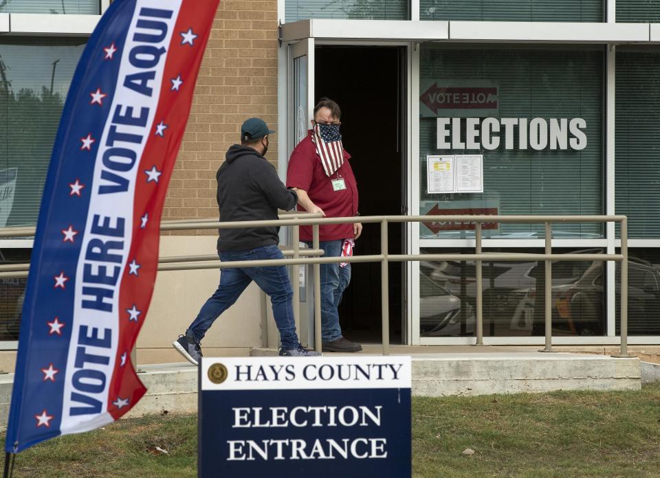 Election clerk Wes Garcia, right, holds the door for a voter Monday at an early voting location at the Hays County Elections Office in San Marcos, Texas. A federal judge late Tuesday ordered that masks be worn in polling places.