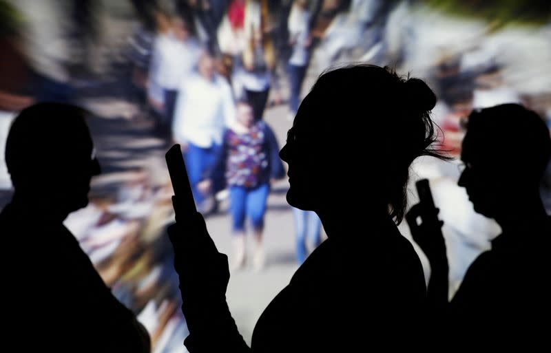 FILE PHOTO: People look at data on their mobiles as background with crowd of people walking is projected in this illustration picture