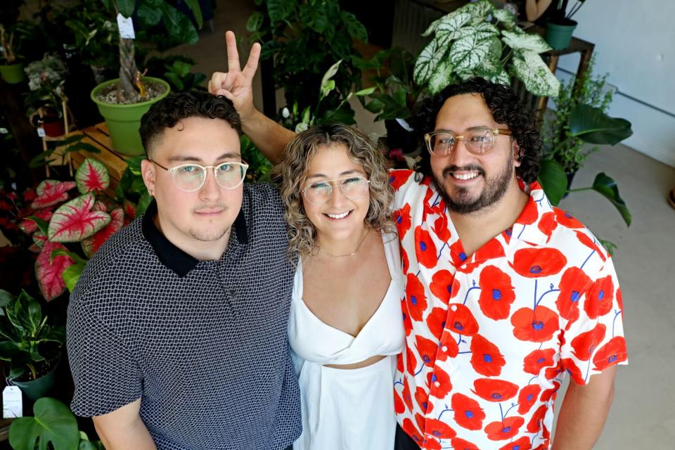 A woman with her arms around two men with plants in the background