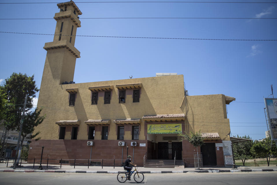 A Palestinian man wears a face mask as he rides a bicycle next to a closed mosque during a lockdown imposed following the discovery of coronavirus cases in the Gaza Strip, Thursday, Aug. 27, 2020. On Wednesday Gaza's Hamas rulers extended a full lockdown in the Palestinian enclave for three more days as coronavirus cases climbed after the detection this week of the first community transmissions of the virus in the densely populated, blockaded territory. (AP Photo/Khalil Hamra)