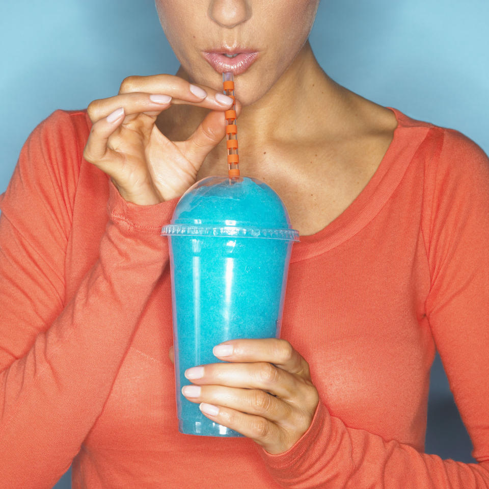 A person wearing an orange shirt sips a blue slushie from a plastic cup