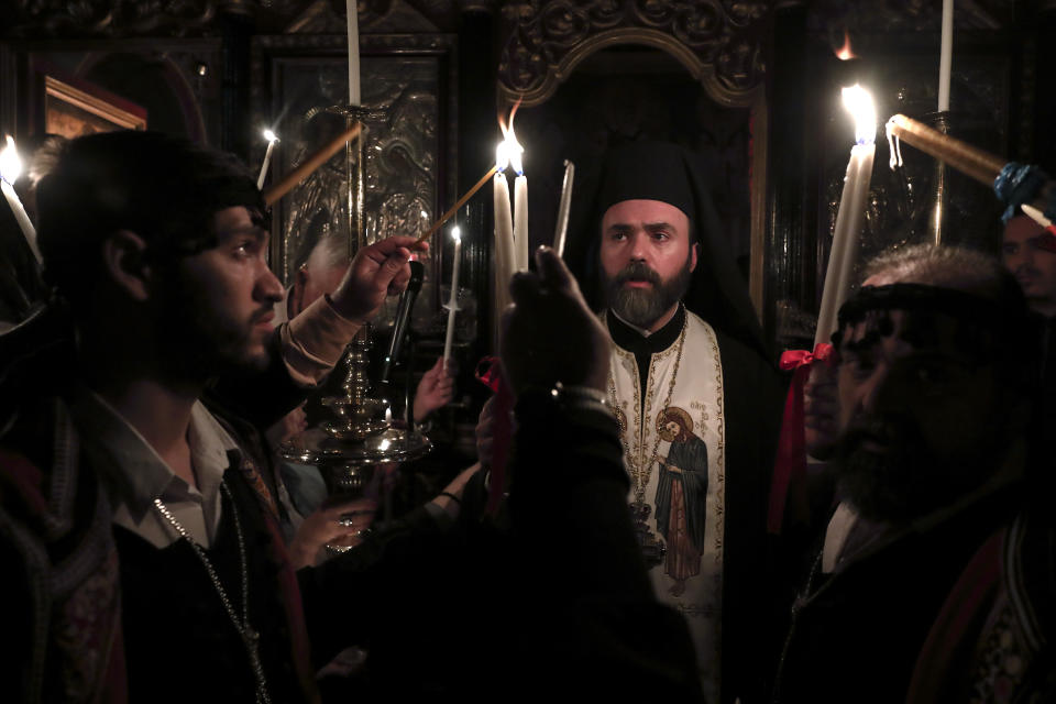 A Greek Orthodox priest lights candles of the faithful with Holy Fire brought from Jerusalem, at a church in Athens, on Saturday, April 27, 2019. A lantern carrying a flame lit in Jerusalem's Holy Sepulcher Church was welcomed in Greece with honors reserved for visiting heads of state. But a senior cleric boycotted the ceremony, miffed that the "Holy Flame" did not land within his see.(AP Photo/Yorgos Karahalis)